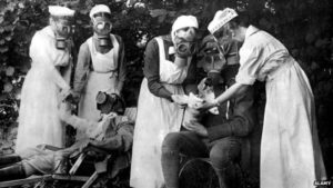 Nurses in gas masks treat soldiers after a gas attack.